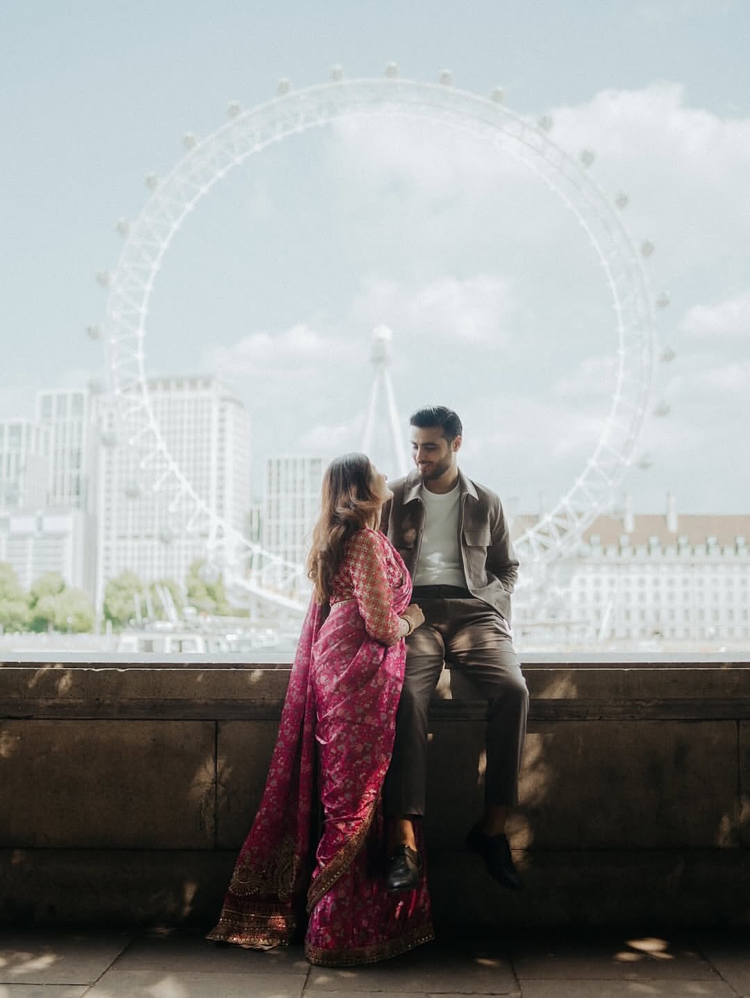 Shailee and Chaitanya seated together with the London Eye behind them